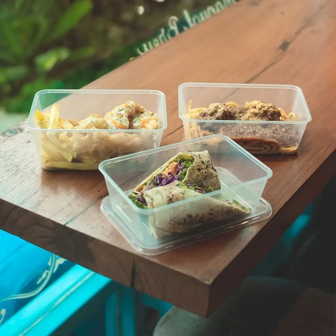 Hộp nhựa chữ nhật trong suốt đựng các món ăn nhanh như gà rán, khoai tây chiên, mỳ Ý và bánh cuộn để trên bàn gỗ
